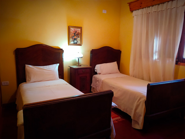 habitación con dos camas vestidas, sommier de madera estilo colonial y paredes color amarillo